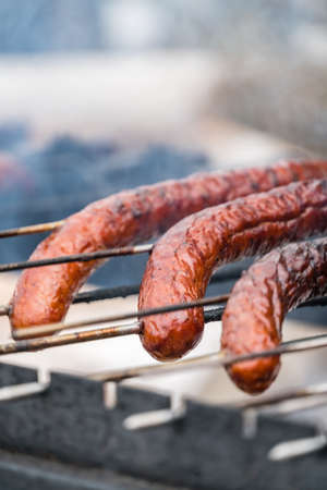 Brown and delicious pork and beef sausages being grilled on a home made turning grillの写真素材