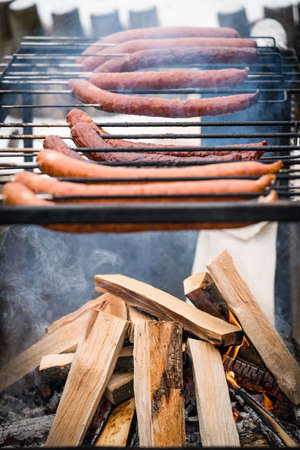 Brown and delicious pork and beef sausages being grilled on a home made turning grillの写真素材