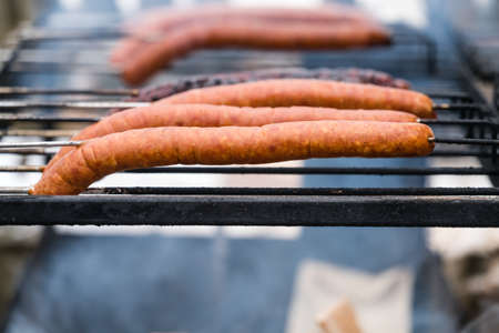 Brown and delicious pork and beef sausages being grilled on a home made turning grillの写真素材