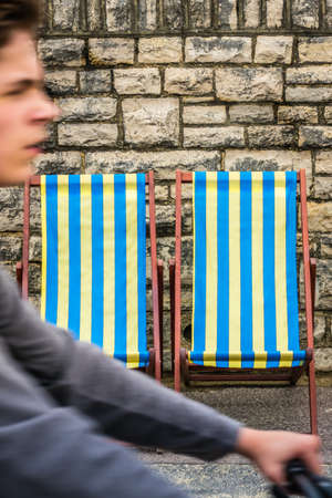 Bournemouth, England -  May 2017 : Man riding on a bicycle in front of the Empty blue and yellow striped deckchairsのeditorial素材