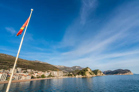Flag of Montenegro fluttering on a mast pole above the stony beach in Petrovac seaside town in spring, Montenegroの写真素材