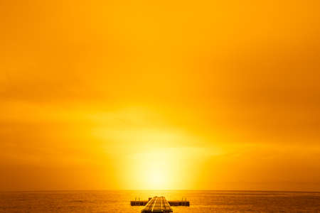 Old empty pier into the calm night sea with sun on the horizon in the backgroundの写真素材