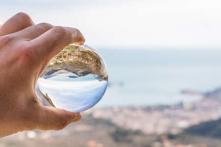 Popular summer resort town Budva on the Adriatic coast in Montenegro reflected in a transparent round sphere ball held by a caucasian manの写真素材