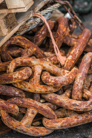 Pile of old, large and heavy rusty chain links in a marina landing in fishing port