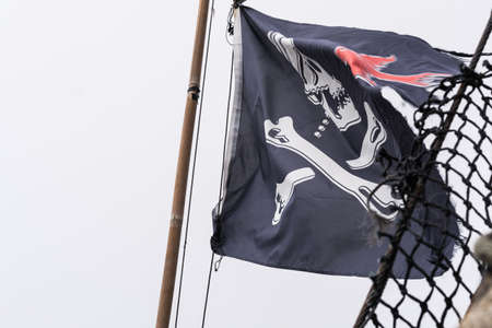 Pirate flag fluttering in the wind on a mast of a pirate ship replica, Penzance harbour, Cornwall, England, UKの写真素材