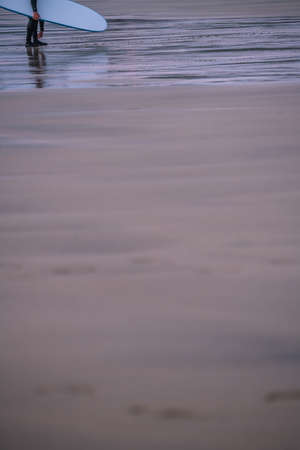 Surfing instructor carrying his surfing board on the beach in Saint Ives, Cornwall, UK