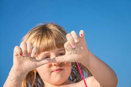 Happy little girl with sandy hands while having fun on the beach in summerの写真素材