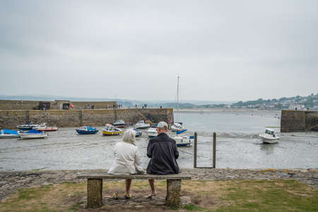 Marazion, England -  May 2018 : Old couple sitting on a bench by the marina in front of St Michaels...