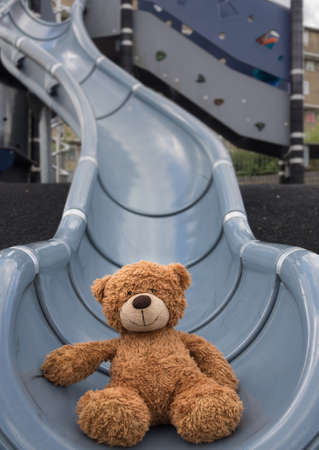 Cute little brown teddy bear at the bottom of big outdoor slide in the playground areaの写真素材