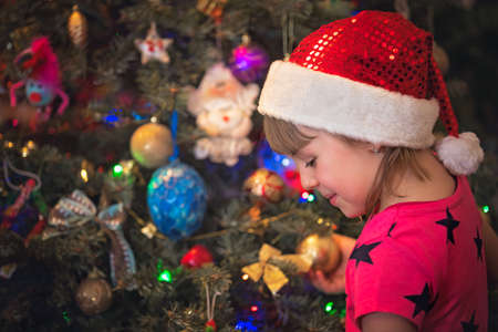 Cute happy and smiling Caucasian Christmas girl putting the decorations on the Christmas treeの写真素材