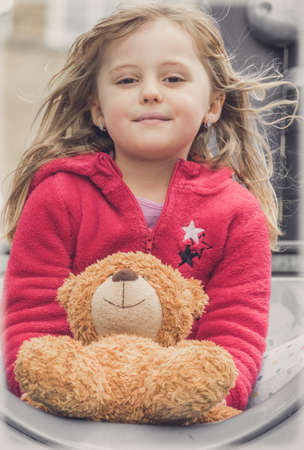 Adorable Caucasian girl holding teddy bear while playing on an outdoor playgroundの写真素材