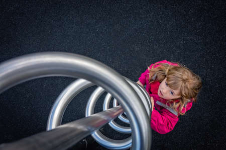 Young Caucasian girl preparing to climb twisted metal swirl on a playgroundの写真素材