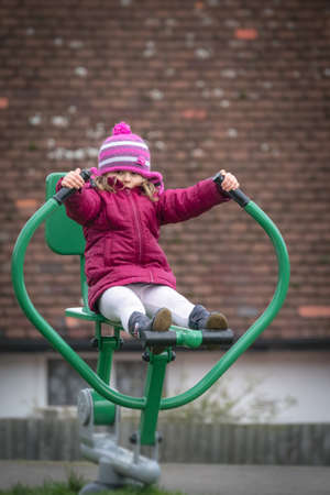 Little Caucasian girl exercising on the outdoor training machine on a chilly autumn dayの写真素材