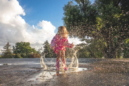 Little Caucasian girl jumping into the puddle after rain in english countryside
