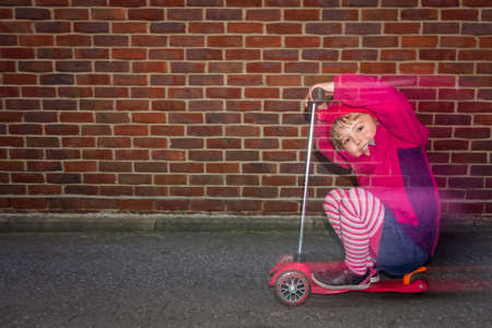 Little Caucasian girl riding fast on her scooter on a road outside her houseの写真素材