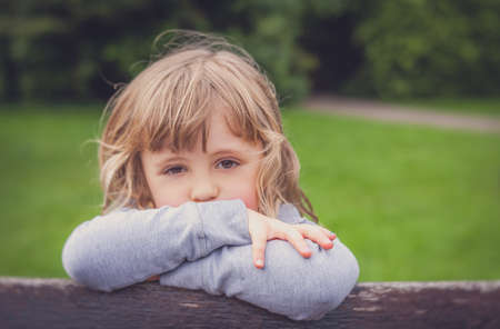 Portrait of a little sad Caucasian girl in a garden in summerの写真素材