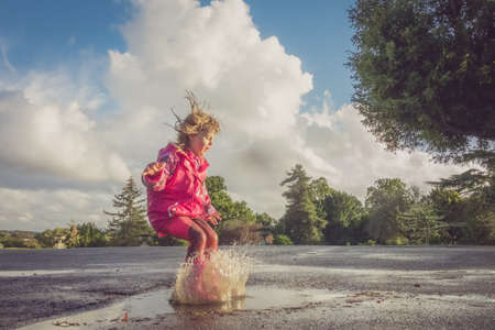 Little Caucasian girl jumping into the puddle after rain in english countrysideの写真素材