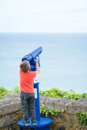 Little boy stretching to to be able to look through the telescope on the viewing platform in...