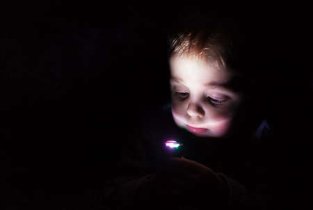 Little Caucasian boy playing with small flashlight in a dark room at homeの写真素材