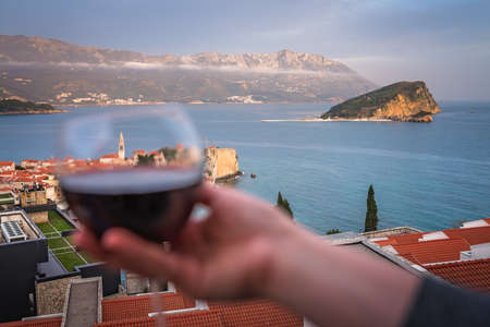 Woman holding glass with red wine on the balcony of her apartment in the Budva town, Montenegroの写真素材