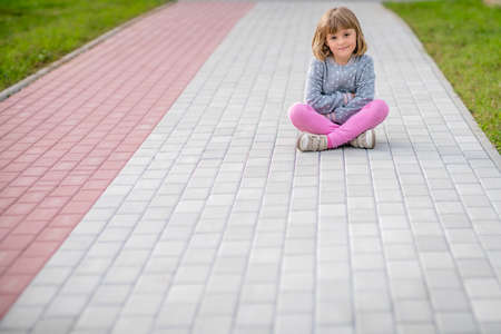 Cute little Caucasian girl sitting on a pavement in townの写真素材