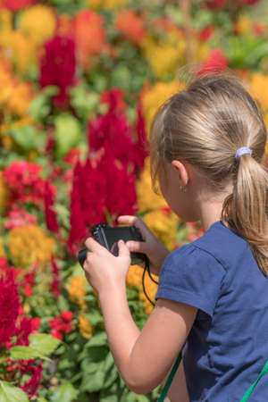 Cute little caucasian girl taking photos of colorful flowers in the park in spring