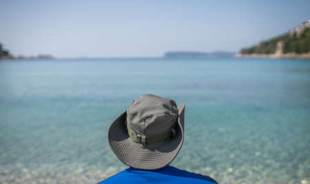 Tourist wearing a hat standing on a beach and looking at the stunning Croatian coast in Dubrovnikの写真素材