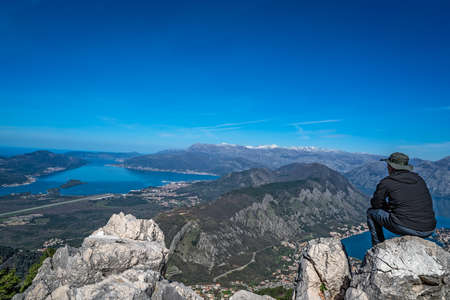 Tourist with a hat sitting on a large boulder and admiring the stunning landscape of the Bay of...