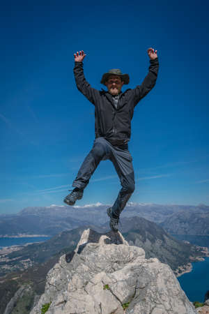 Tourist with a hat jumping high from the large boulder rock in Lovcen National Park, Montenegroの写真素材