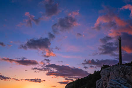 Statue obelisk and Montenegrin flag fluttering in the wind in the fortress on top of cliffs in Petrovac coast at dusk, Montenegroの写真素材