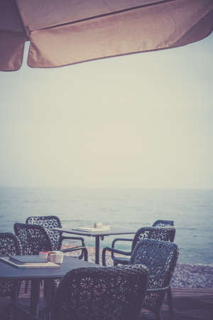Wicker chairs by the empty outdoor restaurant tables at a seaside resort in summerの写真素材