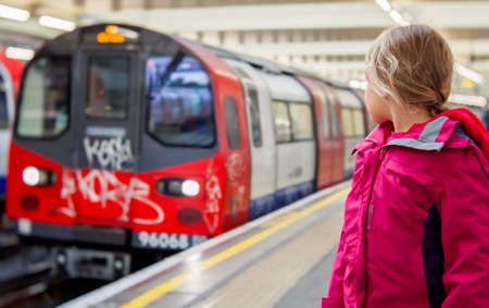 London, England - October 2016 : Little girl standing on the platform and watching the approaching overground train at the stationのeditorial素材