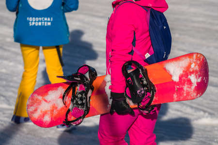 Szklarska Poreba, Poland - February 2019 : Snowboarder dressed in pink ski jacket walking up the slope carrying her snowboardのeditorial素材
