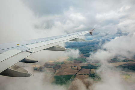 Window view of the wing of an airplane flying above the clouds and english countrysideの写真素材