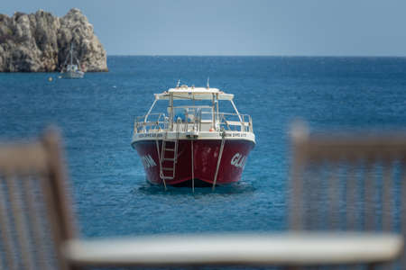Zakynthos, Greece -  April 2019 : Glass bottom boat behind the wooden chairs by the empty outdoor restaurant table on a deck platform in Agios Nikolaos beach, Zakynthos Islandのeditorial素材