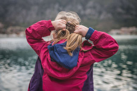 Caucasian girl in a waterproof red jacket standing on the  pier in Kotor Bay and adjusting her hairの写真素材