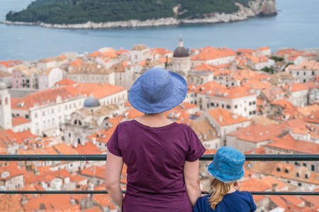 Caucasian Mother and daughter tourists wearnig blue hats standing on top of Old Town Walls in Dubrovnik admiring the view of the historical city below, Croatiaの写真素材
