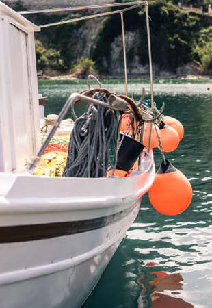 Orange buoys hanging from the side of a small private fisherman boat moored in port near Keri beach...