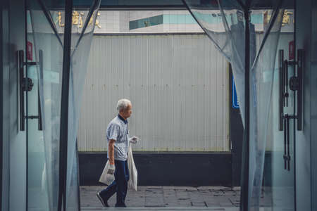 Xian, China -  July 2019 : Old chinese man walking on a street in Xian, photographed from the inside of a shopのeditorial素材