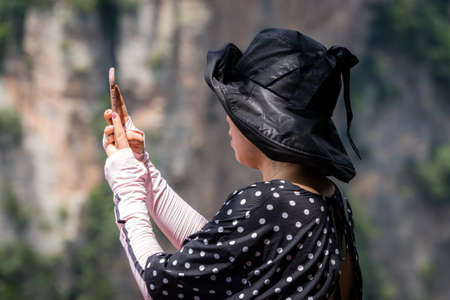 Zhangjiajie, China - August 2019 : Female tourist taking selifie pictures on mobile phone on the  viewpoint in Tianzi mountain range, Avatar mountains nature parkのeditorial素材