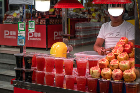 Xian, China -  July 2019 : Man selling plastic cup filled with freshly squeezed pomegranate juice in a stall in Muslim Quarter in Xian town, Shaanxi Provinceのeditorial素材