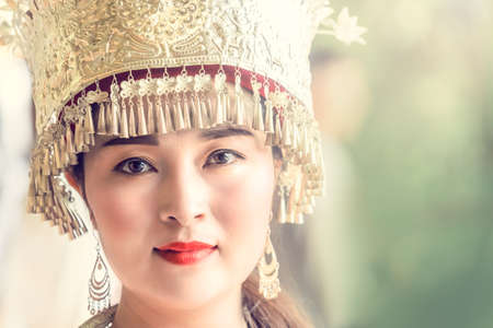 Zhangjiajie, China -  August 2019 : Cultural portrait of a beautiful chinese woman in a traditional chinese dress, wearing a golden decorated hat and standing outdoorのeditorial素材