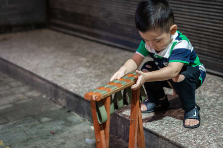 Xian, China -  August 2019 : Cute little chinese boy playing with folding chair outside small local bakery on the street in Muslim Quarterのeditorial素材