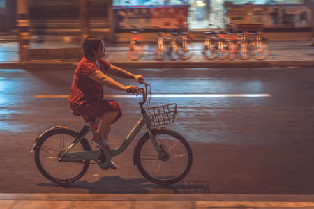 Chengdu, China -  July 2019 : Chinese woman cycling on a bicycle at night on a streetのeditorial素材
