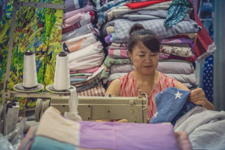 Chengdu, China -  July 2019 : Chinese woman uses electric sewing machine for sewing clothes in her textile shopのeditorial素材