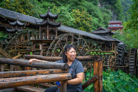 Wullingyuan, China -  July 2019 : Older chinese woman using her legs to pull levers on a wheel of an old Water wheel in Huanglong Yellow Dragon Cave scenic area, Zhangjiajie, Hunan Provinceのeditorial素材