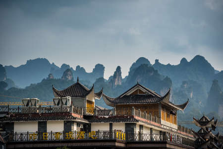 Wulingyuan, China - August 2019 : Rooftops of traditional chinese buildings with the stunningly beautiful rocky karst mountain formations behind as seen from the centre of town, Hunan Provinceのeditorial素材