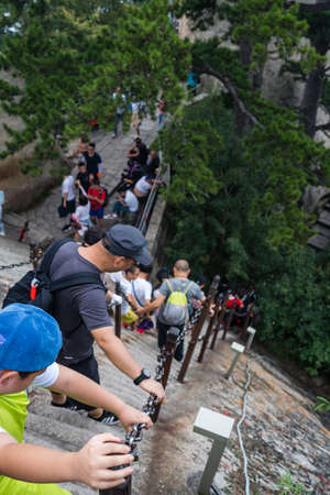 Huashan, China -  August 2019 : Tourists climbing up and descending the stairs on a steep mountain...