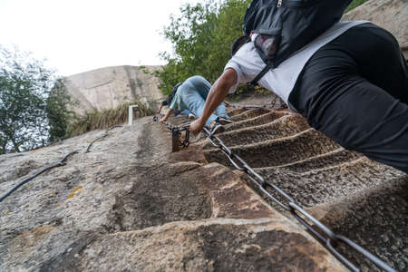 Huashan, China -  August 2019 : Tourist with backpack climbing up the steep, cut into rocky edge stairs on a mountain trail to the North and West Peak on Huashan mountain, Xian, Shaanxi Provinceのeditorial素材