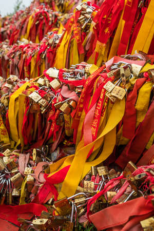 Huashan, China -  August 2019 : Memorial and religious symbolic red ribbons and locked padlocks tied to the barriers along the walking path in Huashan mountain,  Shaanxi Provinceのeditorial素材